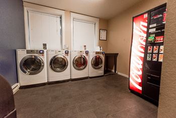 A laundry room with four washing machines and a coca cola machine